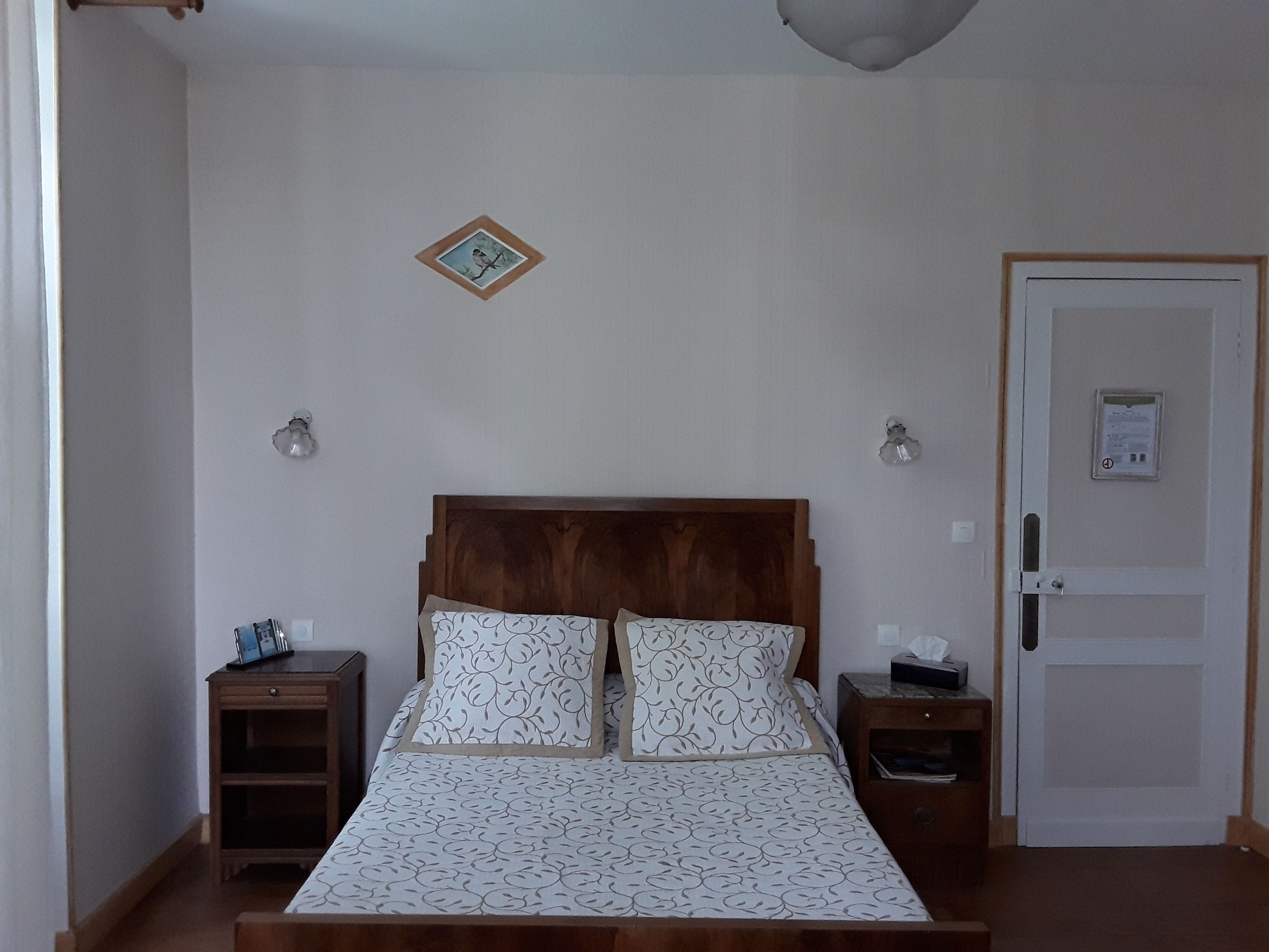 Ein Schlafzimmer mit einem hölzernen Kopfteil, zwei Nachttischen, einem Bett mit gemusterten Betttextilien und einer Tür mit Schloss.