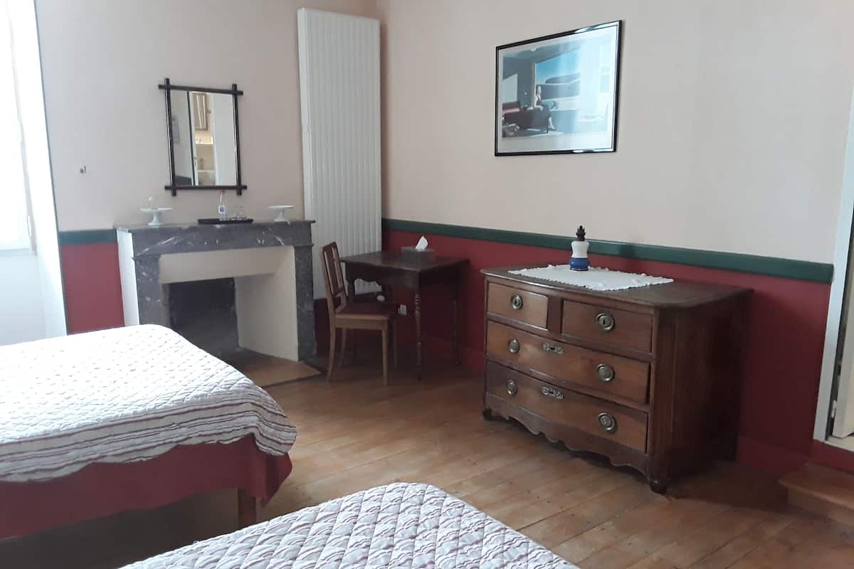 Une chambre avec deux lits, une commode en bois, un bureau et un miroir.