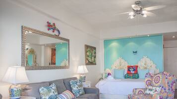 Un dormitorio con una cama, un sofá gris, un sillón estampado, un ventilador de techo y un espejo grande.
