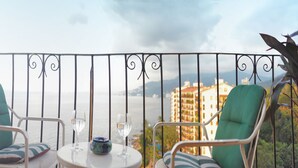 A balcony with two chairs and a table, overlooking a body of water and buildings. - Beach Front Girasol Sur Apartments (Puerto Vallarta)