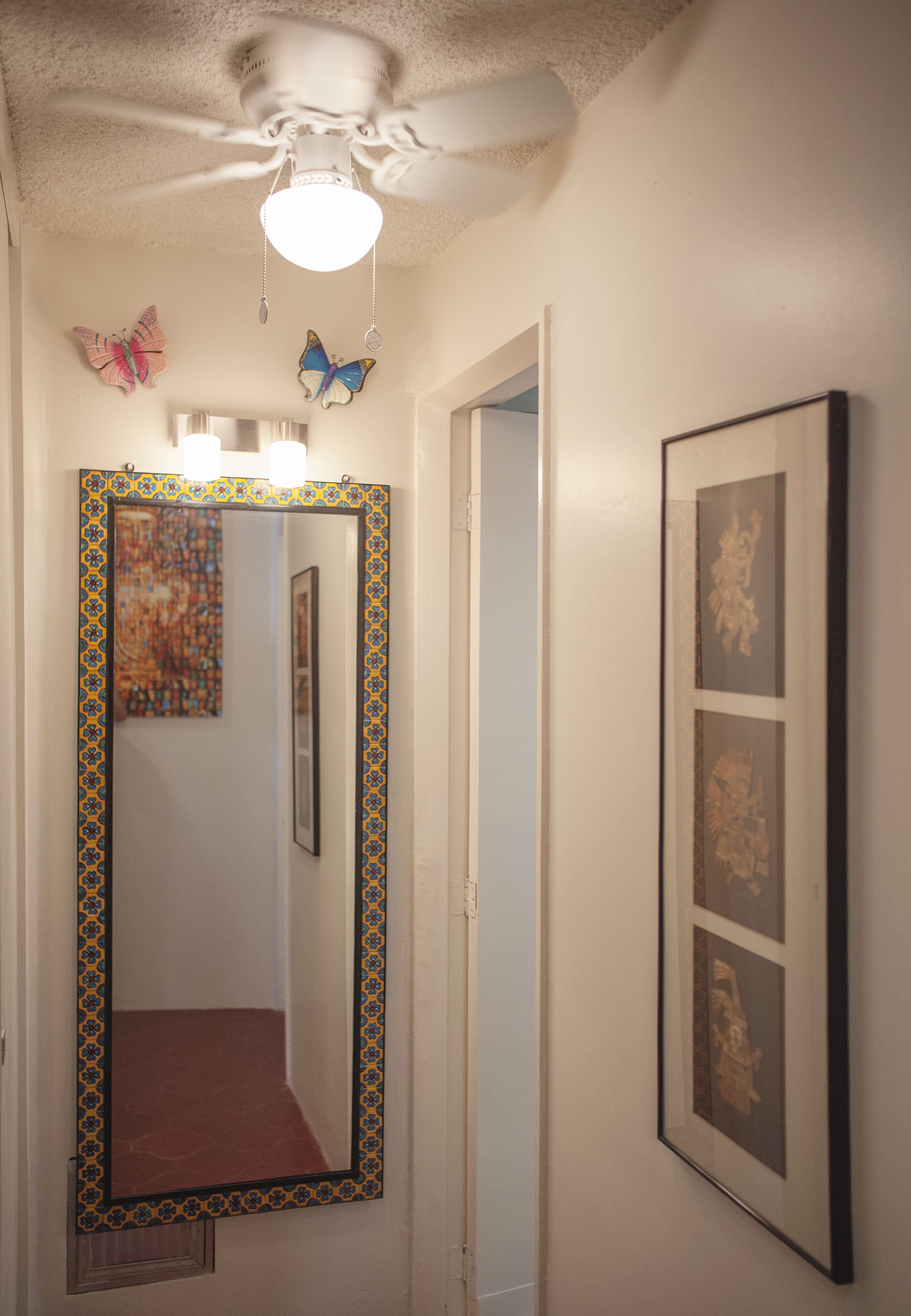 A hallway with a ceiling fan, a mirror with a decorative frame, and a wall with framed pictures.