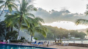 A pool area with palm trees, lounge chairs, and a view of the sea. - Beach Front Girasol Sur Apartments (Puerto Vallarta)
