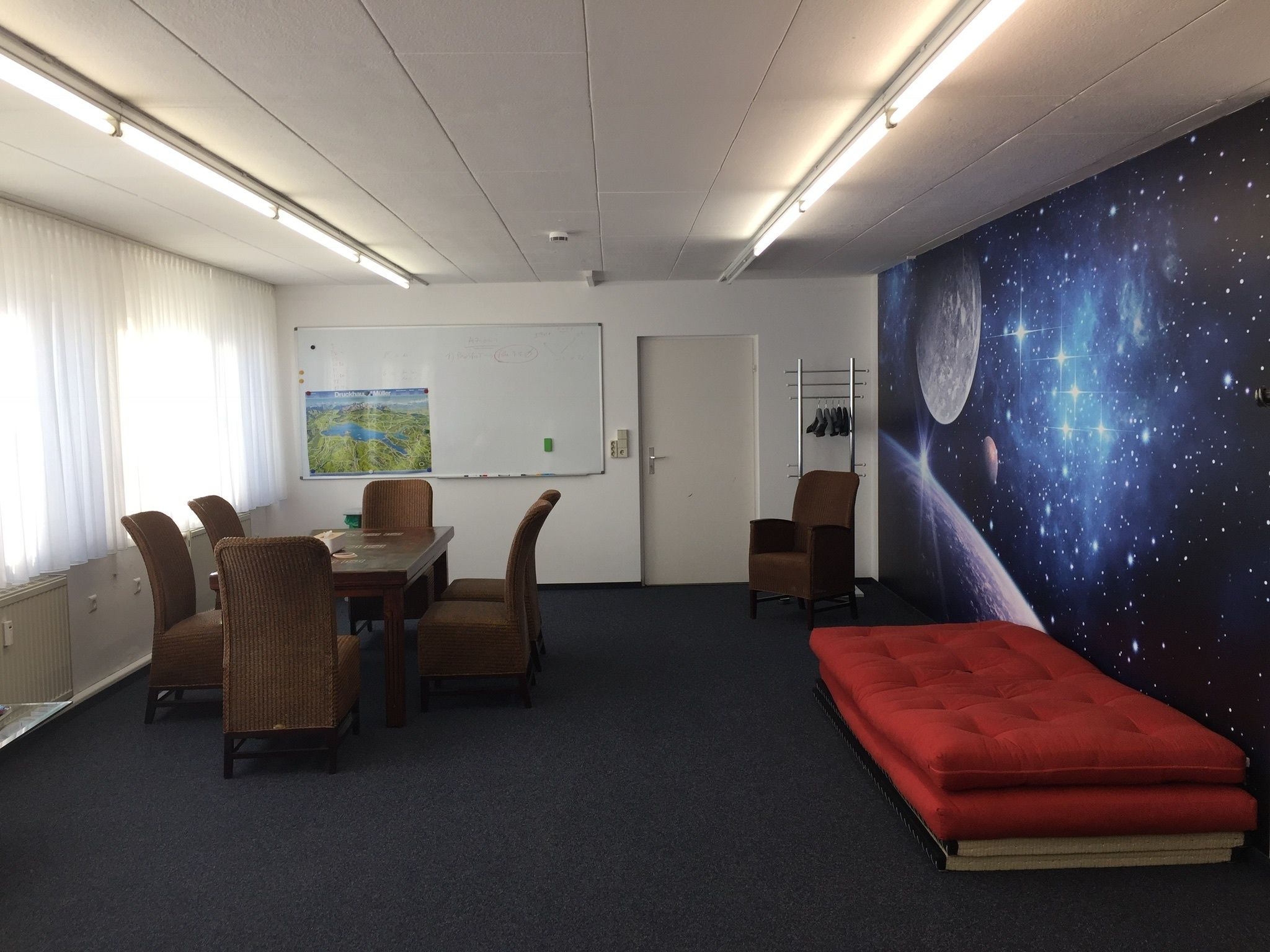 Una sala conferenze con lavagna, tavolo e sedie, un divano rosso e un murale a tema spaziale.