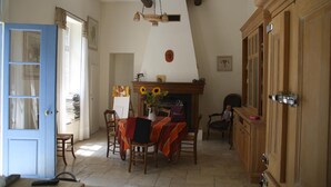 A dining area with a fireplace, wooden furniture, and a blue door. - Aux Pots Bleus (Nissan-lez-Enserune)
