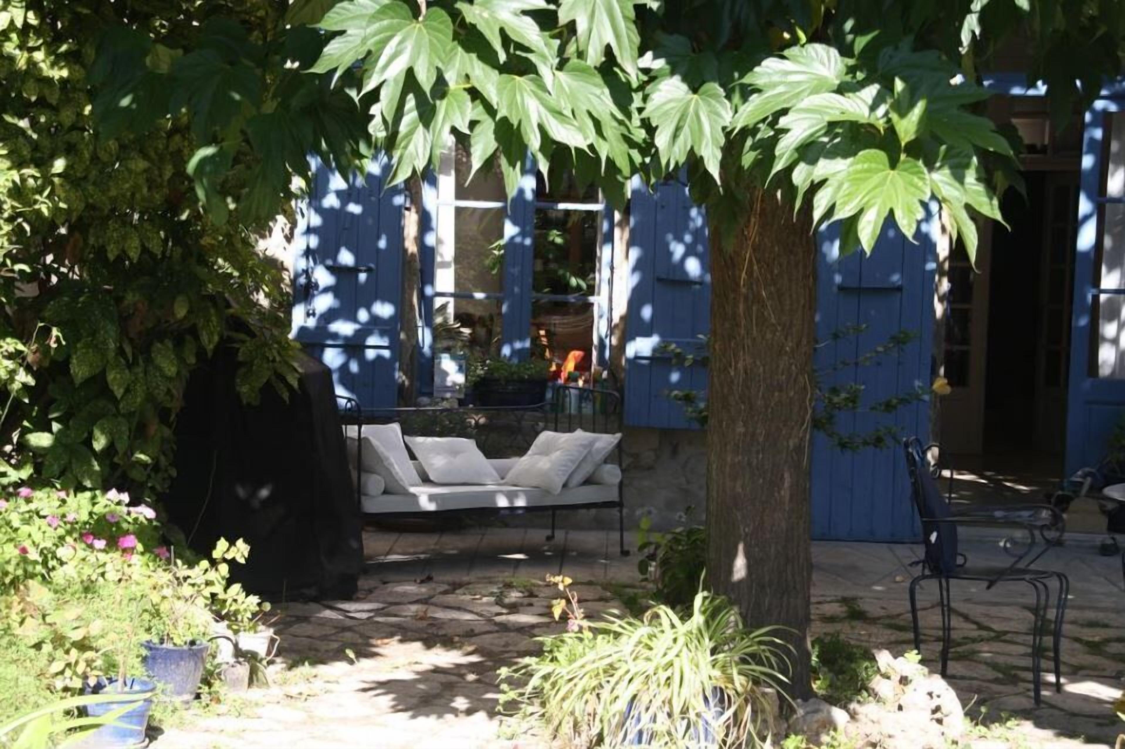 A patio area with a white outdoor sofa, a tree, and potted plants.