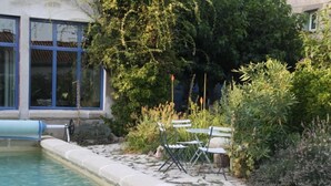 A pool with a stone border, two white folding chairs, and lush greenery. - Aux Pots Bleus (Nissan-lez-Enserune)