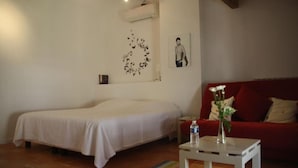 A bedroom with a bed, a red sofa, a small table with a vase, and a wall decoration. - Aux Pots Bleus (Nissan-lez-Enserune)