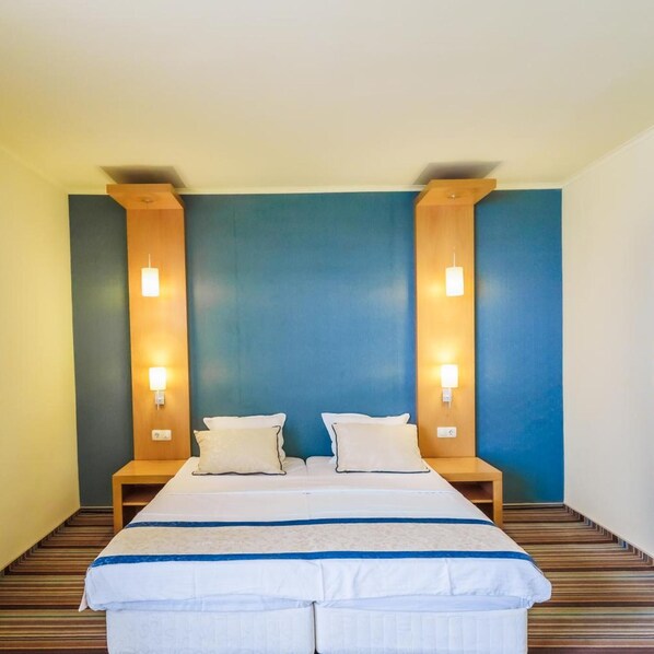 A hotel room with a large bed, two bedside tables, and wall-mounted lamps. - Mirage Hotel (Nessebar)