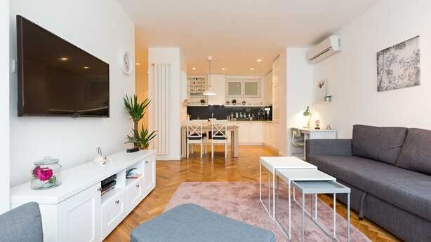 En moderne stue med et fladskærms-tv, en grå sofa og et spiseområde med bord og stole.
