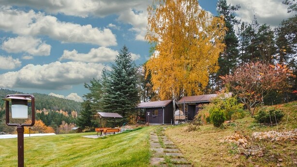 Ein rustikales Blockhaus mit einem Kiesweg, der zu einem Picknicktisch führt, umgeben von Herbstlaub und einem klaren Himmel.