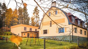 Ein zweistöckiges Haus mit einem geneigten Dach, einem eingezäunten Garten und einer Schaukel.