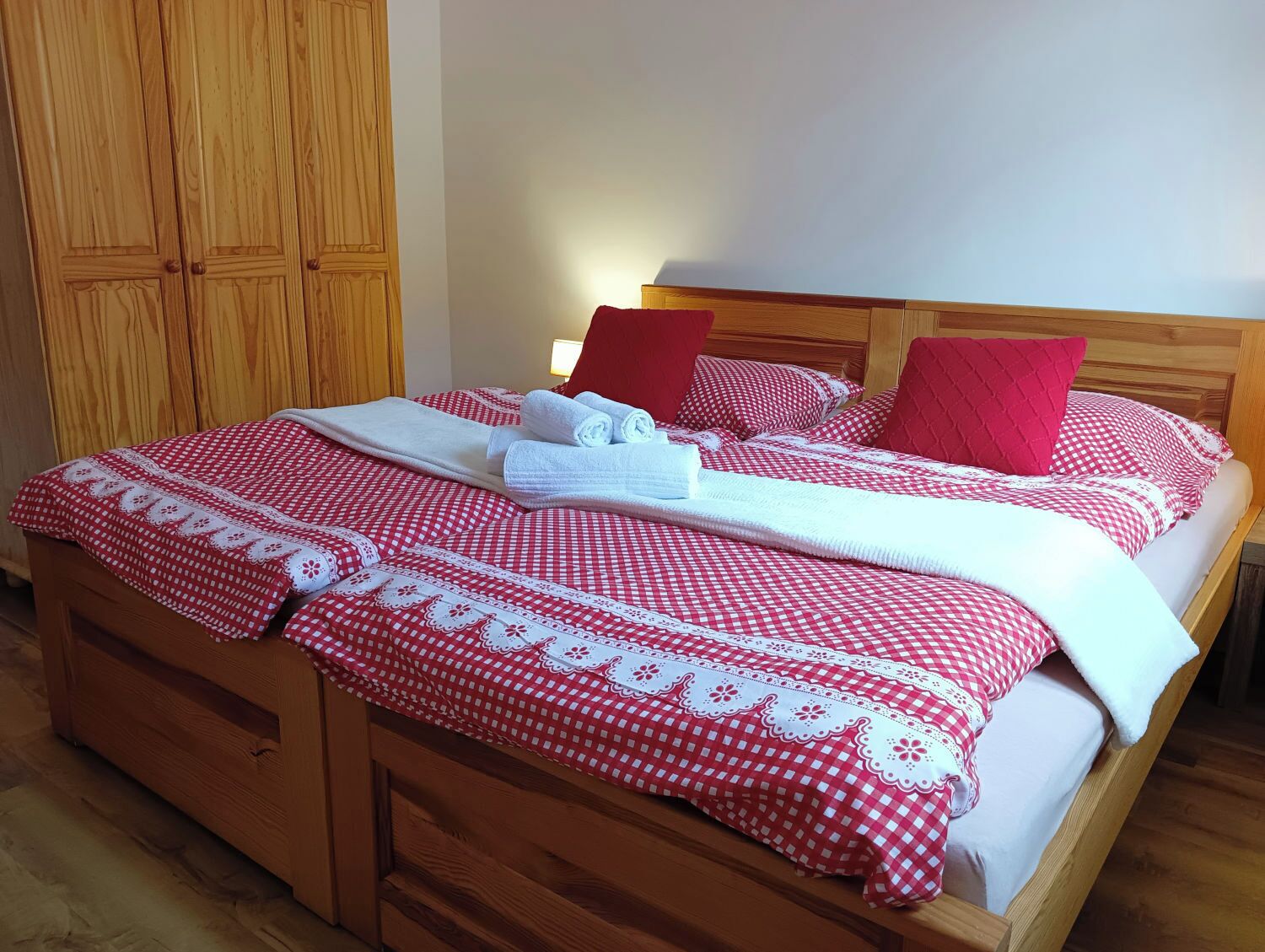 Una cama bien hecha con una colcha de cuadros y almohadas, un cabecero de madera y un armario de madera al fondo.