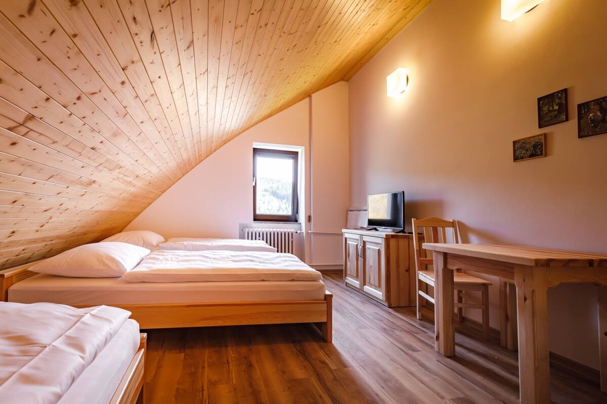 Un dormitorio con techo inclinado, muebles de madera, una cama, un escritorio y un televisor.
