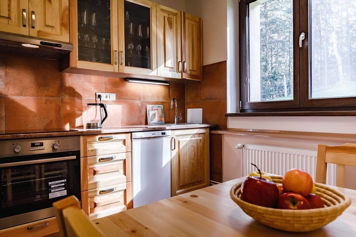 Una cocina con armarios de madera, lavavajillas, horno y ventana con vistas a árboles.