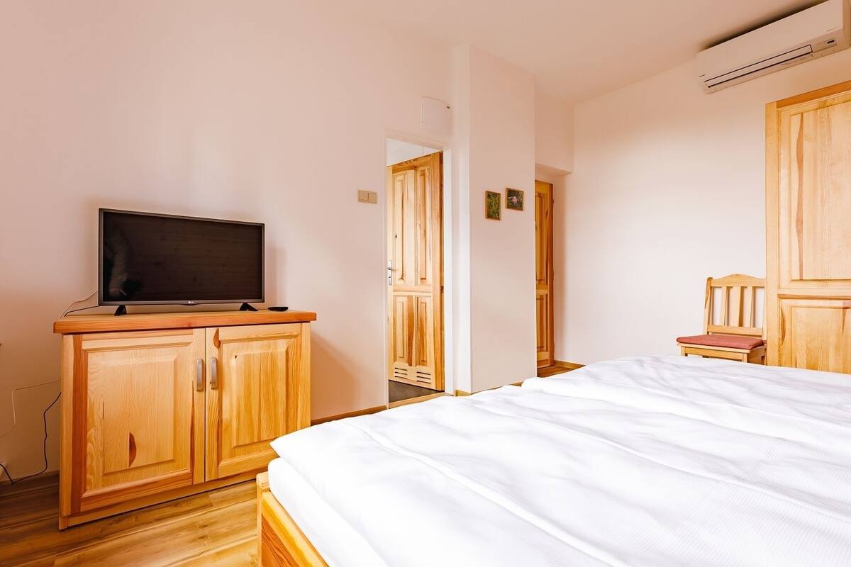 Un dormitorio con un armario de madera, un televisor encima, una cama con ropa de cama blanca y una silla de madera.