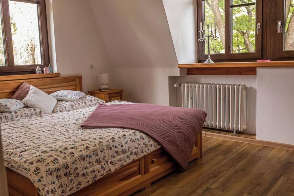 Un dormitorio con cama de madera, un radiador, una ventana con vistas a árboles y una mesita de noche con lámpara.