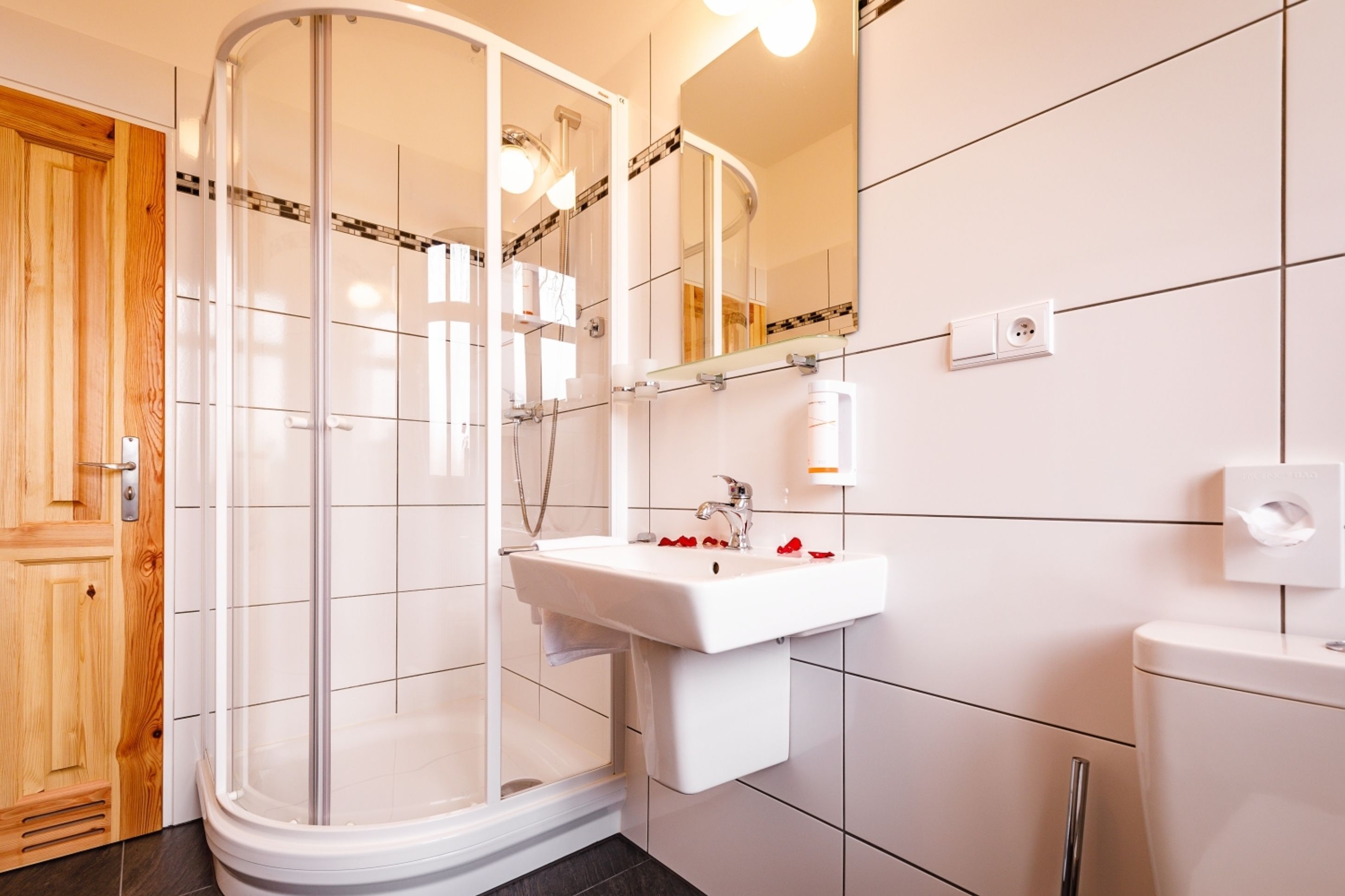 Een moderne badkamer met een douchecabine van glas, een wit wastafelmeubel en een houten deur.