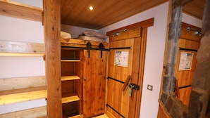 Una habitación de madera con cama alta, un armario y una pared de piedra.