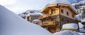 A wooden chalet with stone walls, balconies, and a snow-covered roof, surrounded by a mountainous landscape. - Chalet Monte Bianco (Tignes)