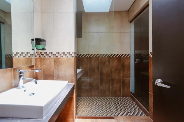 Un baño con un lavamanos blanco, un espejo y una zona de ducha con piso a cuadros.