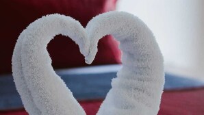 Una toalla doblada en forma de corazón sobre una cama con una etiqueta que dice 'Preservativo Las Maravillas Condom'.