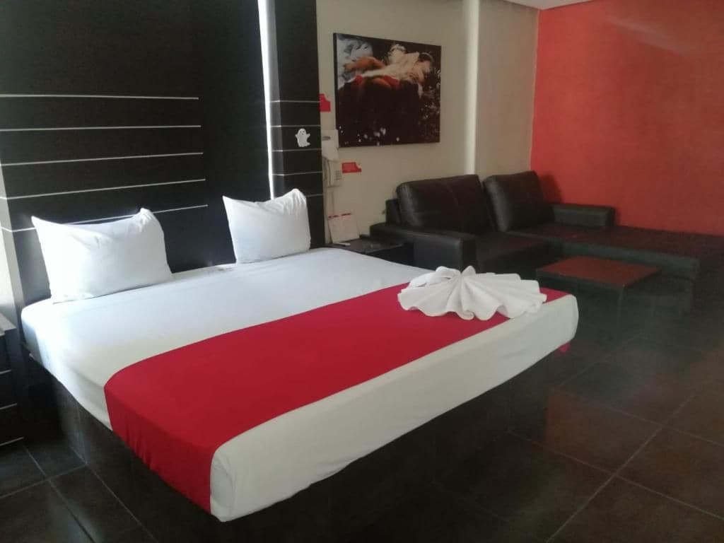 A hotel room with a large bed, a sofa, and a red accent wall.