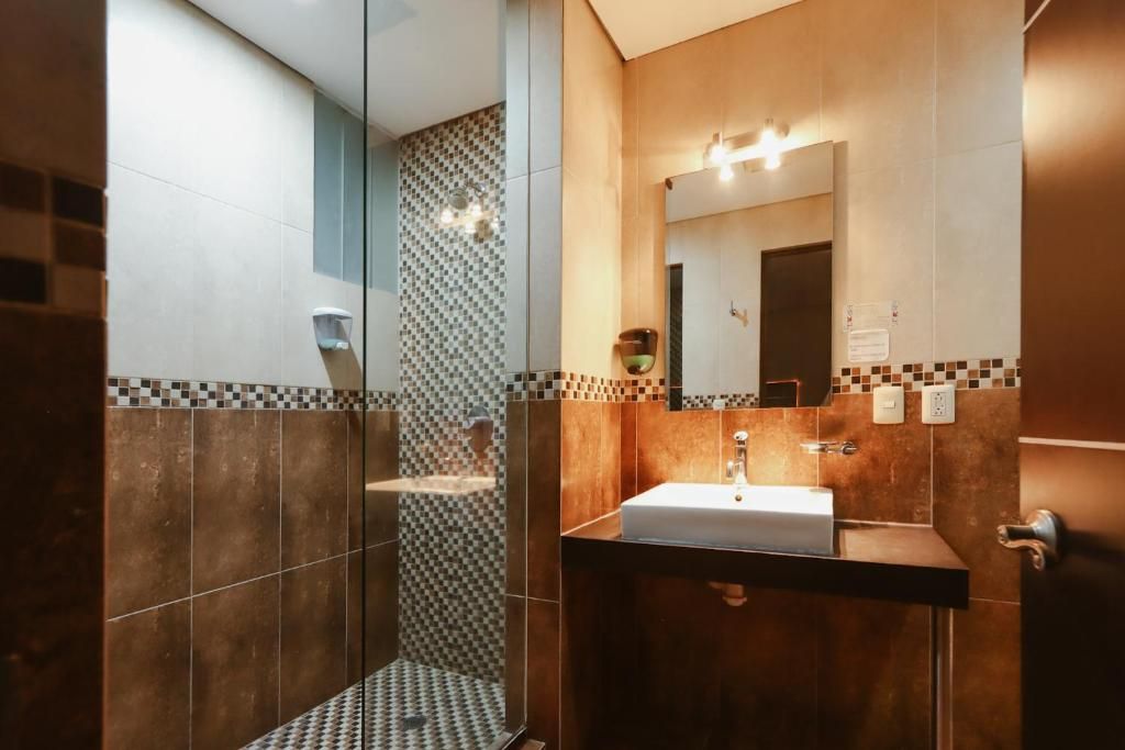 Ein modernes Badezimmer mit einer Duschkabine aus Glas, einem Waschbecken mit Spiegel und gefliesten Wänden.