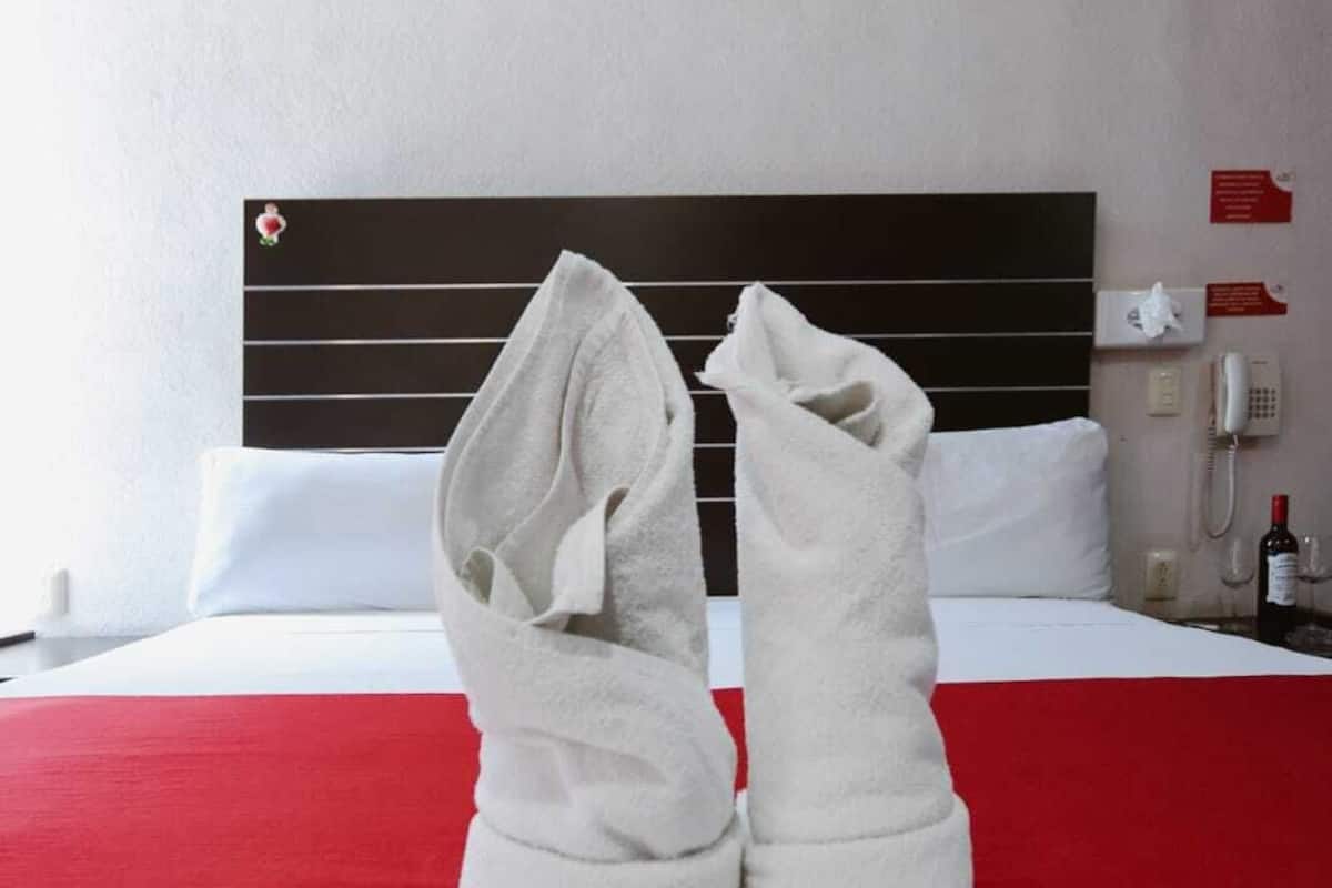 A hotel room with a bed, a red and white bedspread, a white headboard, and a telephone on the nightstand.