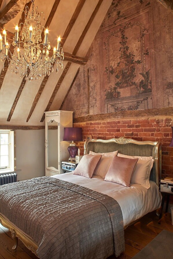 A bedroom with a bed, chandelier, and a brick wall with a fresco. - Broad Leys (Aylesbury)