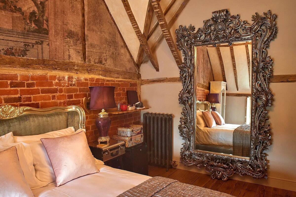 A bedroom with a large ornate mirror, a bed with pillows, a dresser, and a radiator.