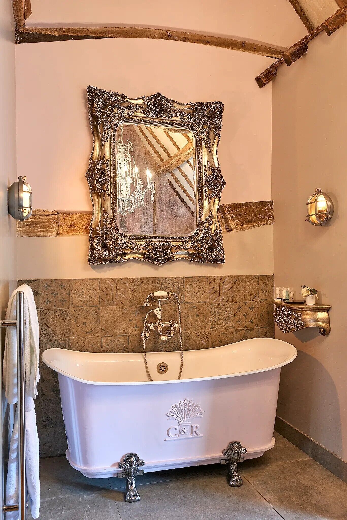 A bathroom with a freestanding bathtub, a large ornate mirror, and a wall-mounted vanity with a light fixture.