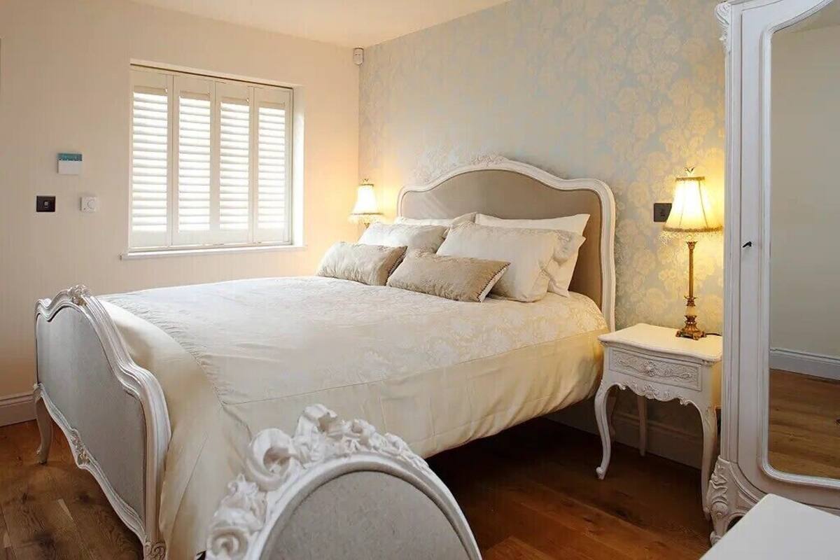 A bedroom with a bed, two bedside tables, a window with shutters, and a mirror.