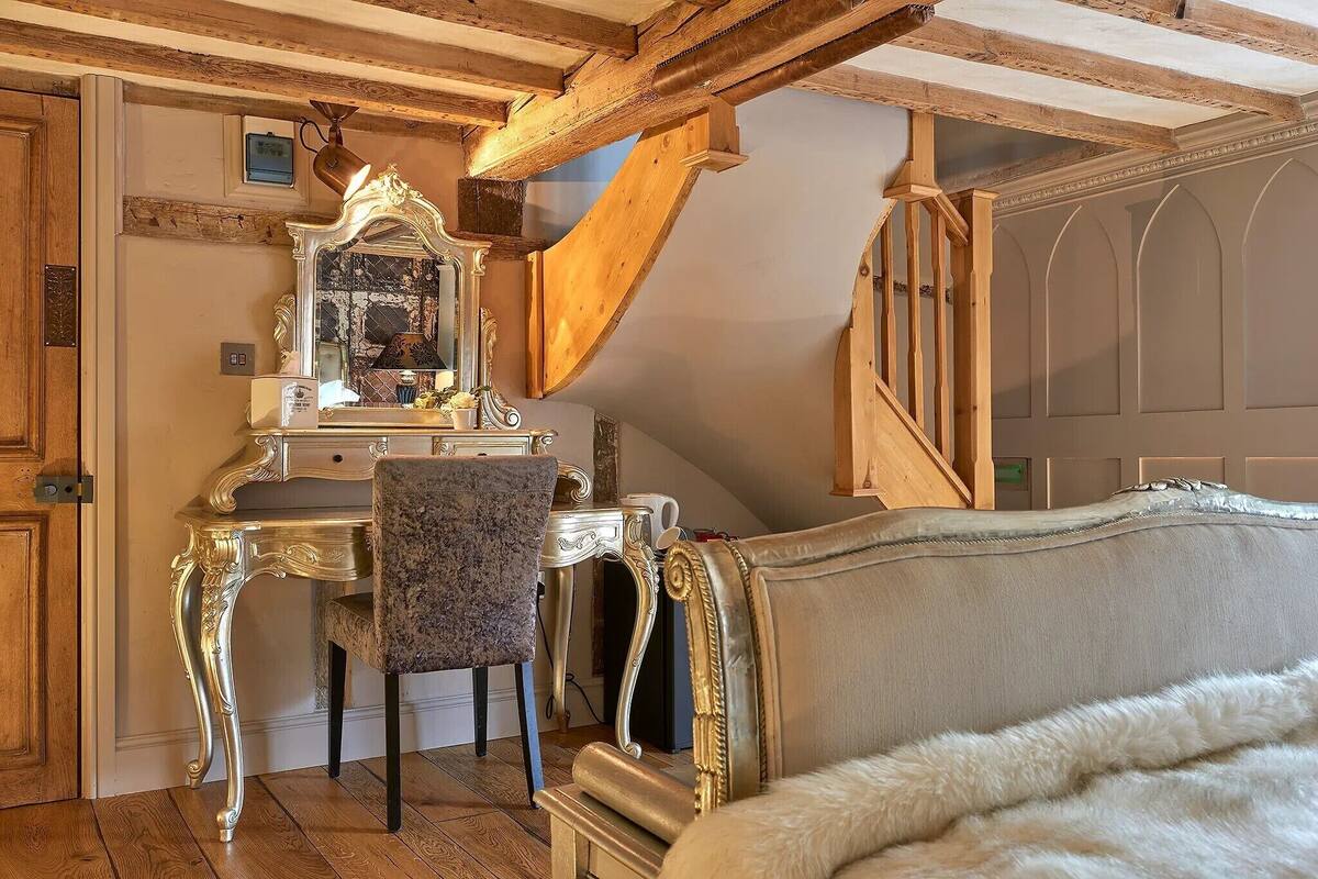 A room with a wooden ceiling, a vanity with a mirror, a chair, and a sofa.