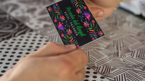 Una mano sosteniendo una tarjeta negra con diseños florales coloridos y texto.