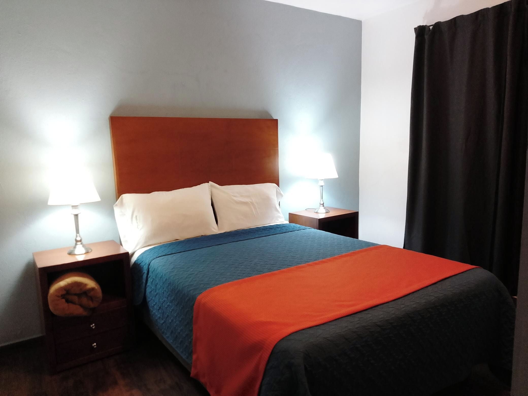 A hotel room with a bed, two bedside tables, a lamp on each table, and a black curtain.