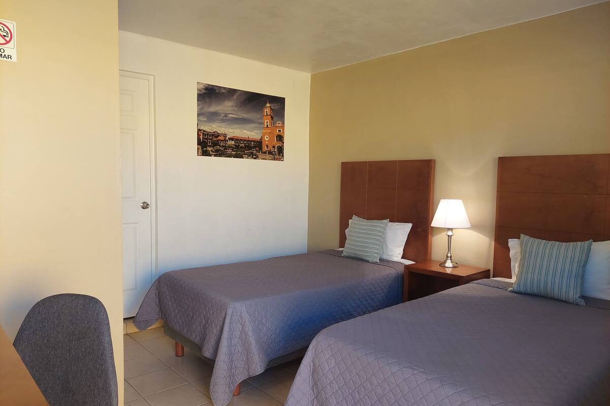 A hotel room with two beds, a desk, and a chair.