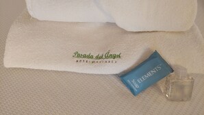 A neatly folded white towel with embroidered text, a blue Elements soap bar, and a clear shampoo bottle on a textured surface. - Posada del Ángel (Mineral de la Reforma)
