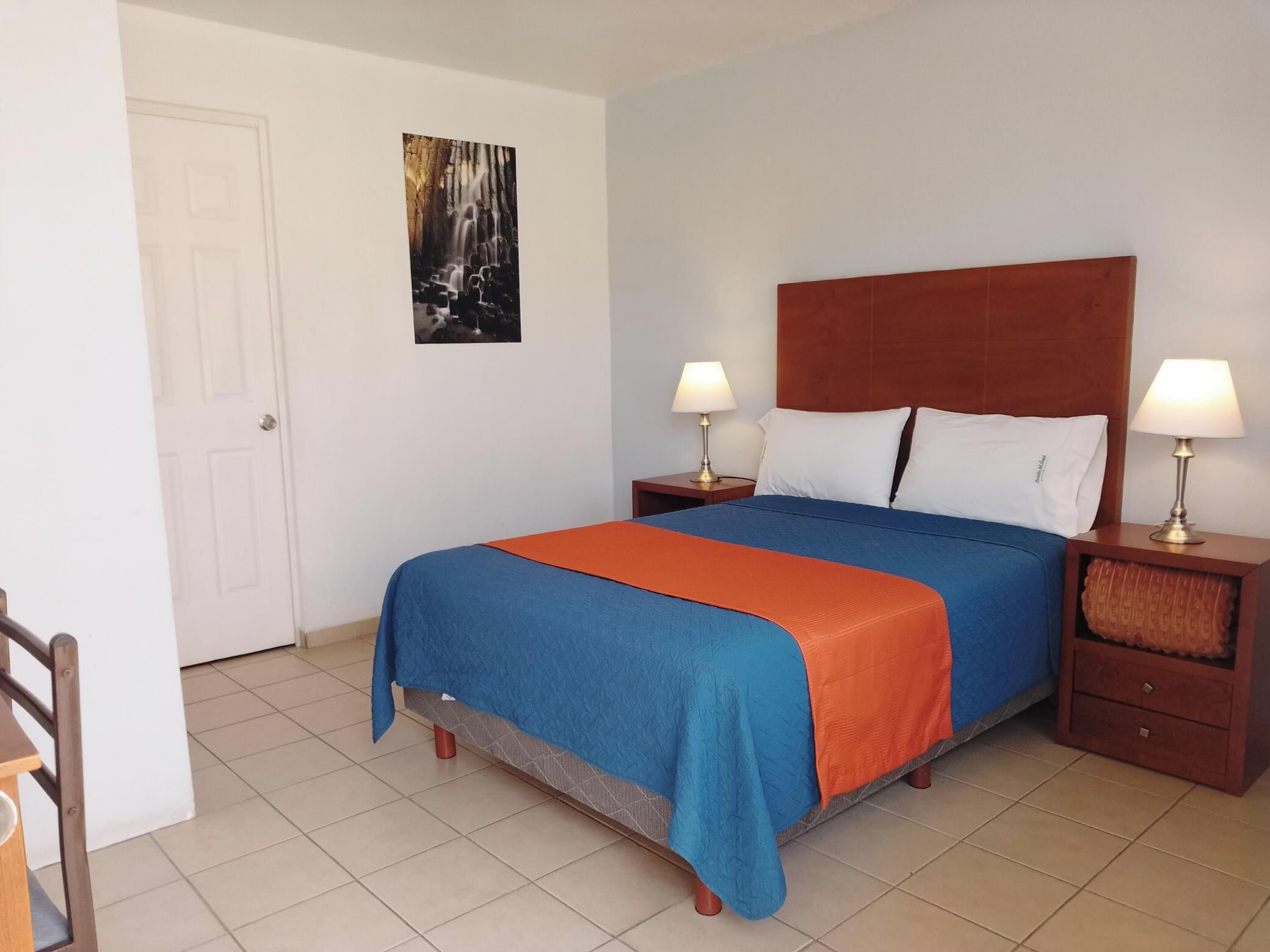 A hotel room with a bed, two bedside tables with lamps, a door, and a wall-mounted picture.