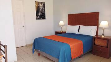 A hotel room with a bed, two bedside tables with lamps, a door, and a wall-mounted picture.