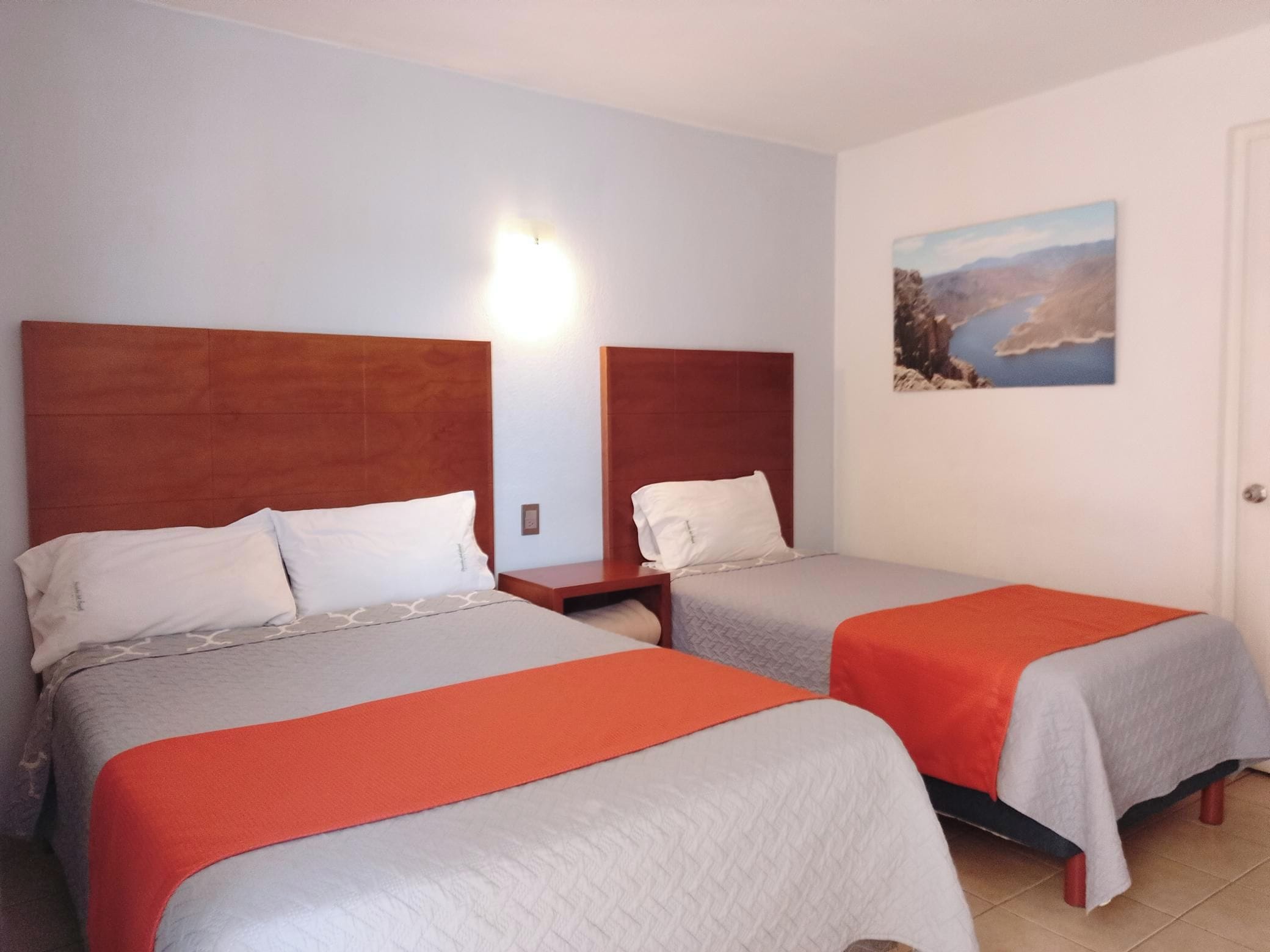 Une chambre d’hôtel avec deux lits, chacun doté d’une tête de lit en bois, d’une table de chevet et d’un tableau au mur.