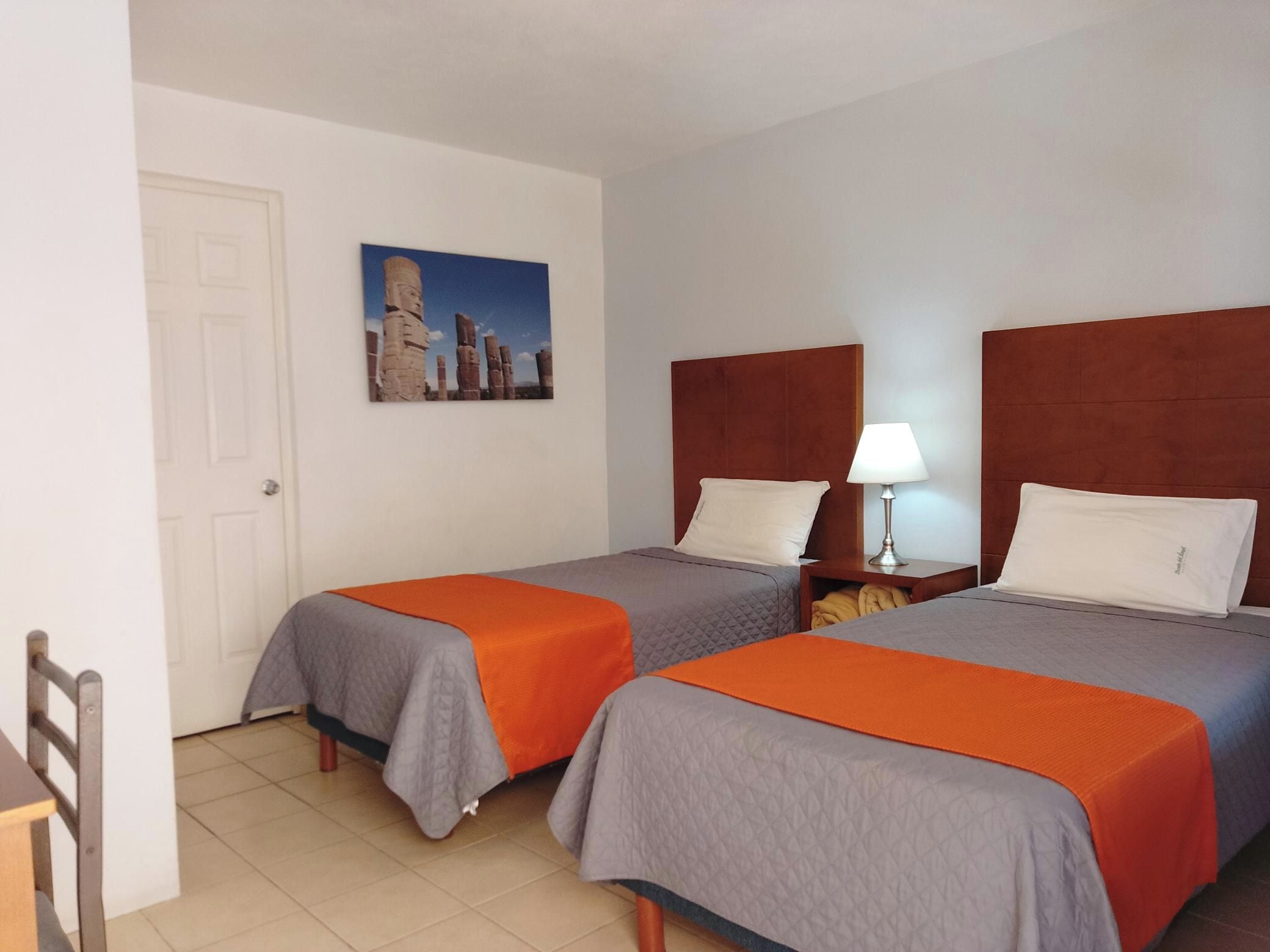 Een hotelkamer met twee bedden, een nachtkastje, een lamp en een deur.