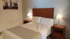 Habitación de hotel con una cama grande, dos mesitas de noche con lámparas, cabecera y un cuadro en la pared.