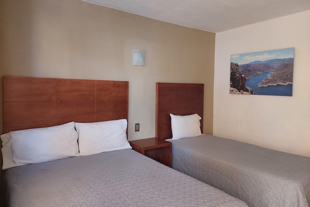 A hotel room with two beds, each with a wooden headboard and white pillows. There is a painting of a landscape on the wall.