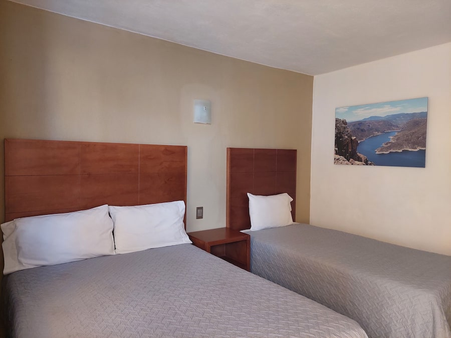 A hotel room with two beds, each with a wooden headboard and white pillows. There is a painting of a landscape on the wall.