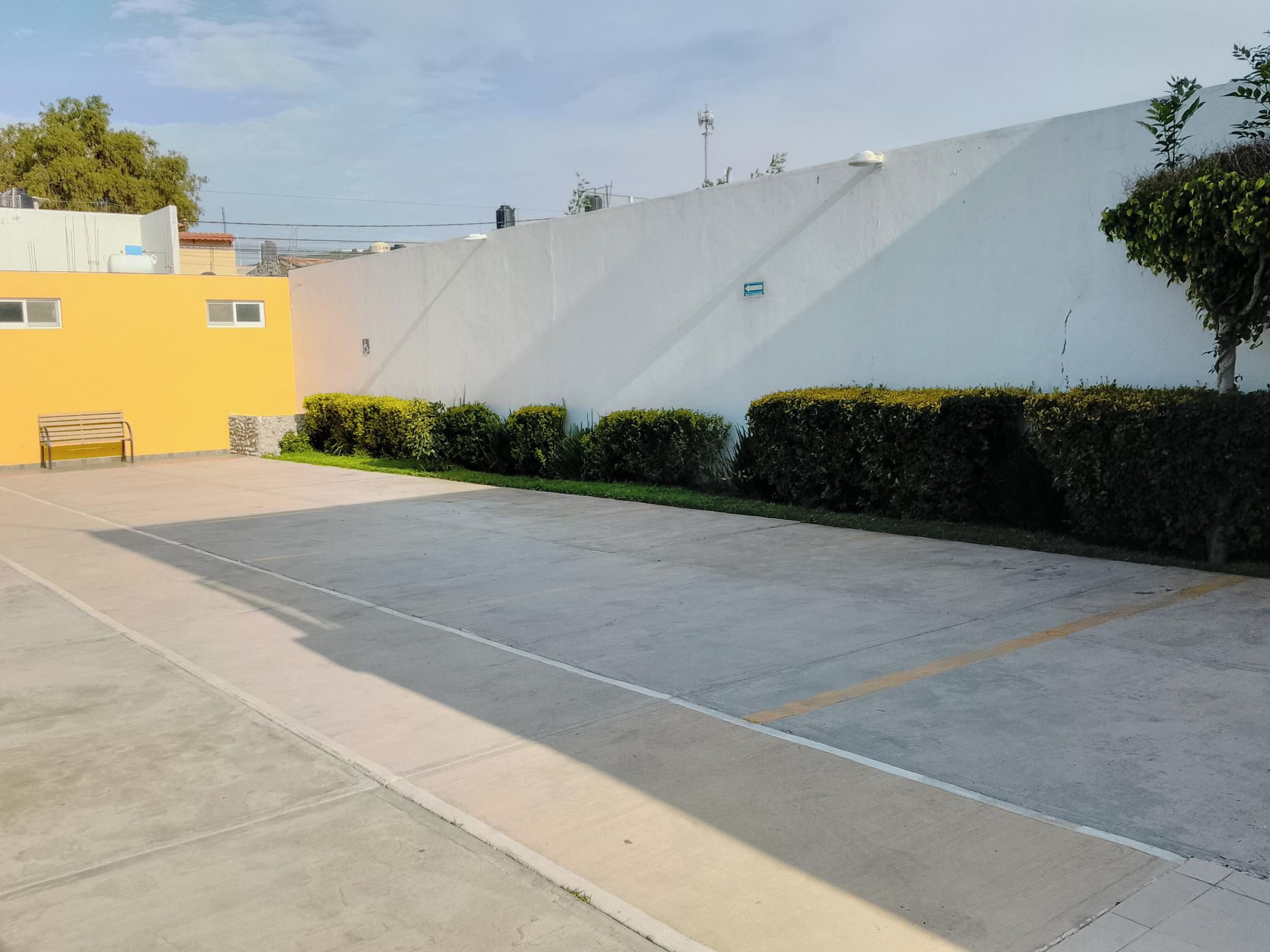 Een vlak, open parkeerterrein met een geel gebouw en een witte muur op de achtergrond.