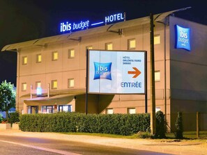 Un hotel con un cartel que indica 'ibis budget hotels' y una señalización apuntando a 'ENTREE'.