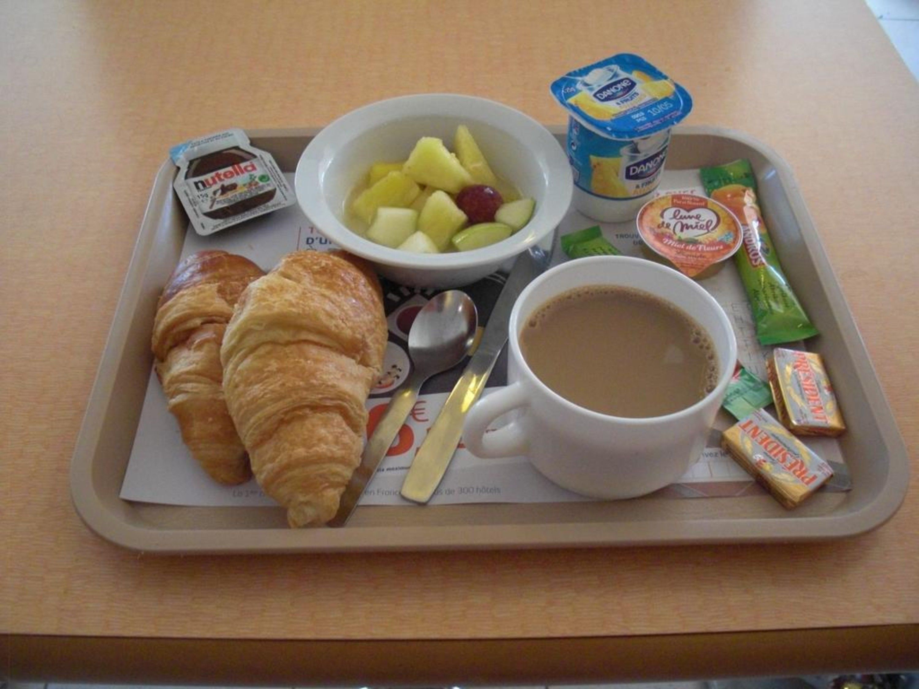 A tray with croissants, a bowl of fruit, yogurt, and a cup of coffee.