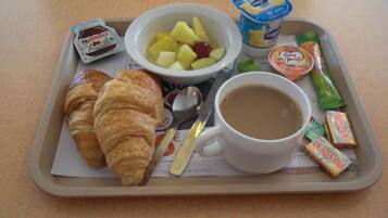 A tray with croissants, a bowl of fruit, yogurt, and a cup of coffee.