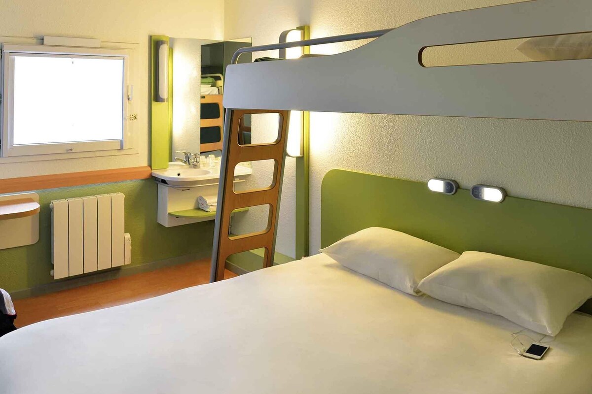 A bunk bed with a ladder, a bedside table, a mirror, a window, and a radiator.