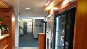 Un couloir avec des distributeurs automatiques, une plante et une porte donnant sur une autre pièce.